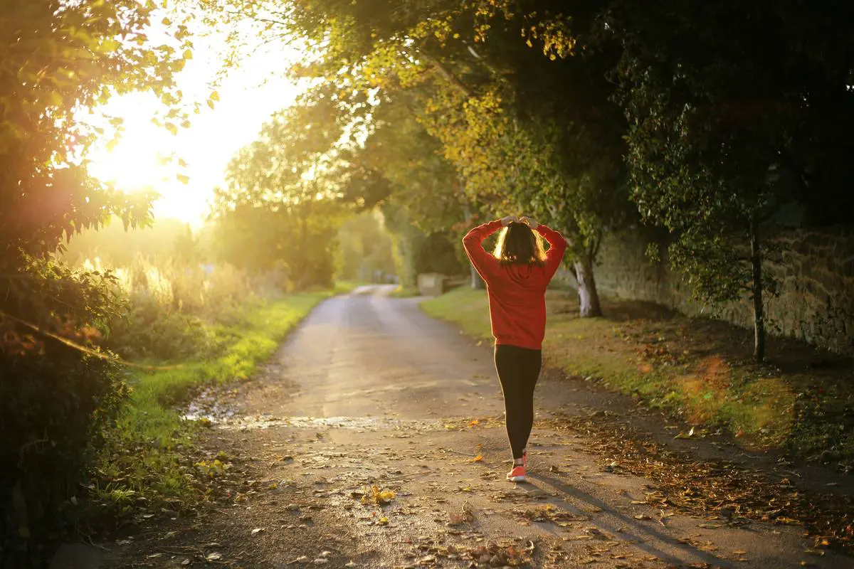 Mindfulness and relaxation A woman walking down a sunlit tree-lined road at golden hour, practicing mindfulness and relaxation