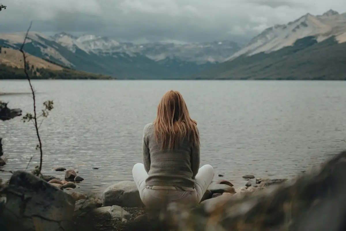 Connecting with nature A woman sitting peacefully by a mountain lake gazing at the still water, connecting with nature to find calm in a chaotic world