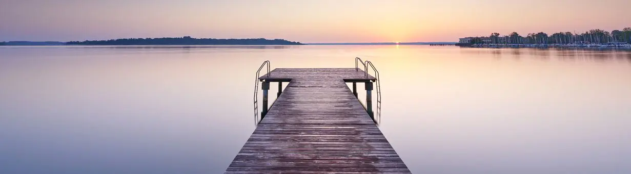 Finding calm amid uncertainty A quiet wooden dock stretching over a still lake at sunset, evoking calm and peace amid uncertainty