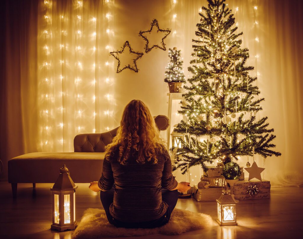 Girl meditating in a tree lit room by Christmas Tree